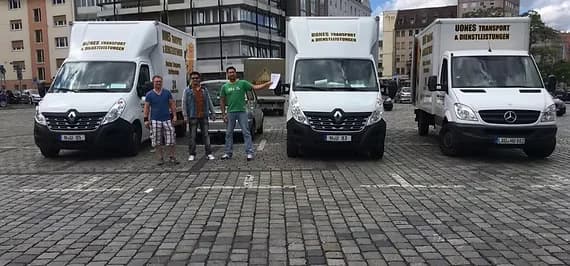 Drei Mitarbeiter stehen neben drei UONES-Kofferfahrzeugen auf einem gepflasterten Platz